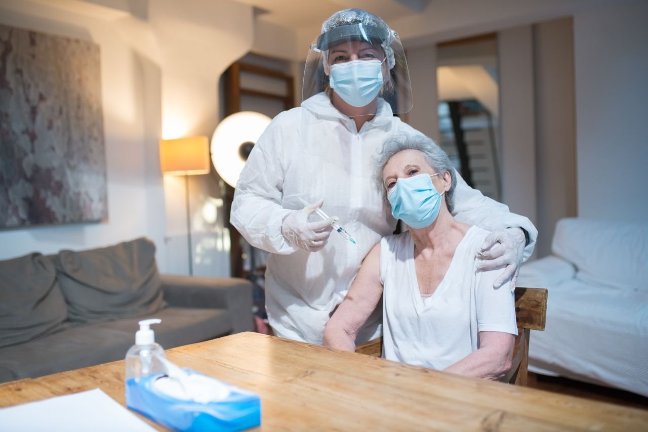 about-img A healthcare worker in protective gear gives a vaccine to a senior woman at home.